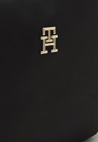 Borsa a tracolla in nylon nero con un evidente dettaglio logo in metallo dorato. La texture è liscia con una silhouette elegante.