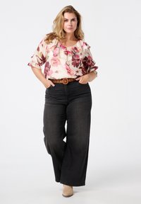 Bloemige blouse met gerimpelde halslijn in roze en paarse tinten, gecombineerd met hoge zwarte wijde jeans en een bruine riem.