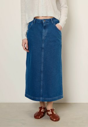 Denim maxi skirt in medium blue with a straight shape, two front pockets, and a front seam. Paired with red strappy sandals.