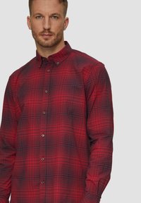 Rood en marineblauw geruite blouse met kraag, lange mouwen en een textuurstof met kleine knopen aan de voorkant.