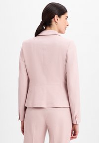 Lichtroze op maat gemaakte blazer met een gestructureerde vorm, textuurstof, ingeknipte kraag en knoop manchetten. Gladde afwerking, achteraanzicht weergegeven.