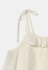 Top sin mangas blanco con un escote volado, tirantes ajustables y una tela texturizada con líneas verticales.