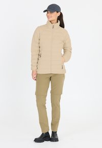 Beige pufferjacka med dragkedjefickor, dragkedjestängning och hög krage; kombinerad med ljusbruna cargobyxor och svarta ankelkängor.