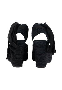 Sandalias de cuña negras con suelas de yute trenzado, talones abiertos y cintas de tela como correas para el tobillo. Superficie texturizada con un acabado suave.