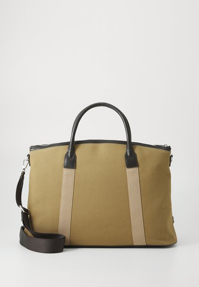 Sac fourre-tout en toile beige avec des accents en cuir noir, deux poignées supérieures et une bandoulière amovible. Fermeture zippée, surface texturée.
