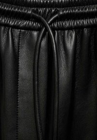 Les joggeurs en cuir noir présentent une taille à cordon de serrage, une texture douce et un grain subtil, avec des plis rentrés le long des côtés pour un détail supplémentaire.