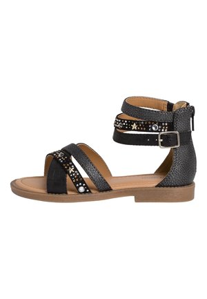 Black flat sandal with ankle strap, buckle, zipper back, and decorative studs and star-shaped embellishments on the straps.