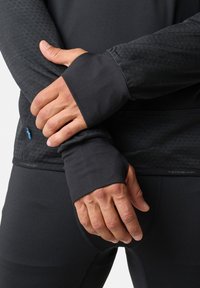 Zwart sporttop met lange mouwen en leggings, voorzien van duimgaten. Gestructureerde stof met een subtiel patroon. Logo zichtbaar nabij de zoom.
