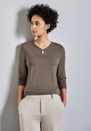 Top marrón de manga larga con un detalle de cuello en forma de ojo de cerradura, combinado con pantalones ajustados de color beige claro. La tela parece suave, con un diseño entallado.