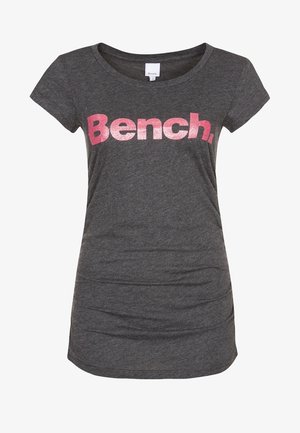 Szary t-shirt z krótkim rękawem, okrągłym dekoltem oraz grafiką na przodzie z napisem „Bench” w błyszczących różowych literach. Gładka tekstura materiału.
