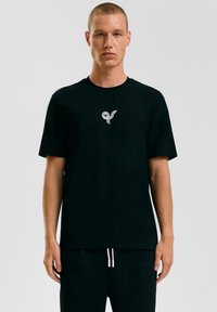 Zwarte katoenen t-shirt met korte mouwen, voorzien van een grijs logo op de linkerborst. Het ontwerp is eenvoudig met een ronde hals.