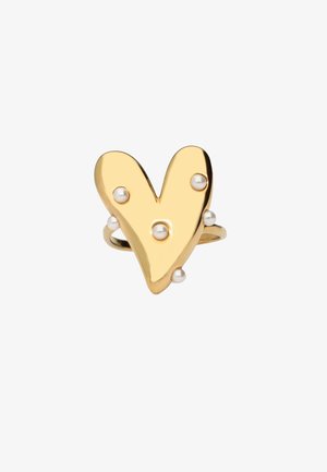 Anillo de oro con una forma abstracta de corazón adornado con seis pequeñas perlas blancas sobre un fondo blanco liso.