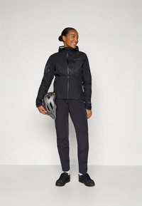 Black waterproof jacket with a hood, featuring a zipper and side pockets. Paired with black pants and a gray bike helmet.