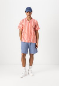 Kortærmet skjorte med koralstriber, blå shorts, hvide sneakers og en blå kasket. Bomuldsstof, afslappet pasform og uformelt design.