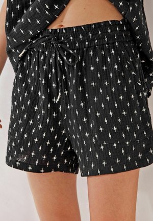 Short en tissu noir avec de petits losanges blancs, une taille élastique avec un cordon et une grande poche avant à droite.