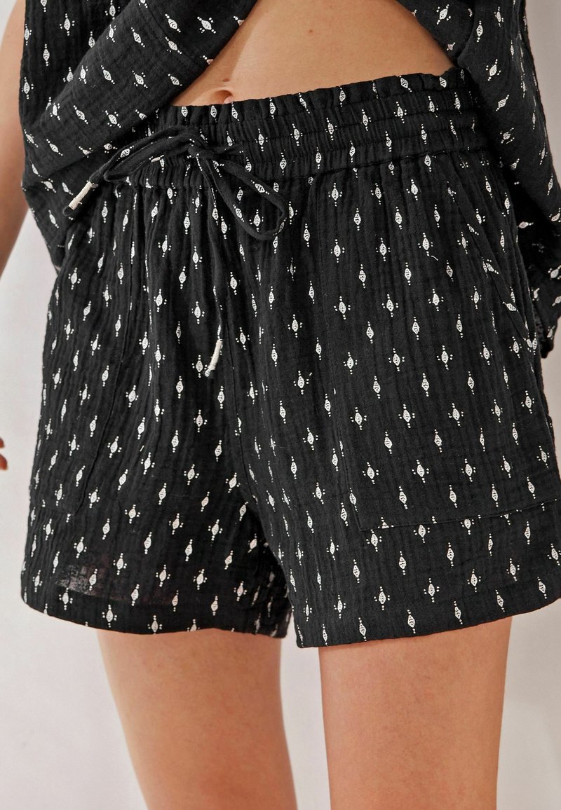 Short en tissu noir avec de petits losanges blancs, une taille élastique avec un cordon et une grande poche avant à droite.