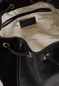 Musta nahkainen saalislauku, jossa on kullanväriset metalliosat, beigenvärinen sisustuskangas toistuvalla logokuvioinnilla, kiristettävä nyörisulkija.