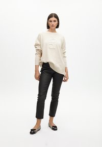 Maglione oversize color crema con dettaglio del logo, abbinato a pantaloni in ecopelle neri aderenti e ballerine con motivo che presentano un'accento a fiocco.