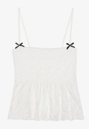 Fehér csipkeborítású camisole vékony pántokkal, fekete masnikkal a vállakon, és fodros alsó résszel a nőies megjelenésért.