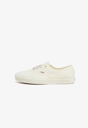 White canvas sneakers with pink shoelaces, low profile, round toe, Vans logo on side, stitched accents, and rubber sole.
