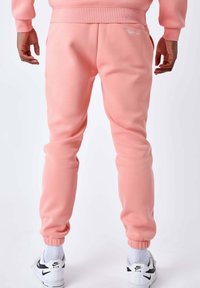 Rosa Fleece-Jogginghosen mit elastischem Bund und Knöchelbündchen, versehen mit einem kleinen weißen Logo an der linken Hüfte. Kombiniert mit weißen Nike-Sneakern.