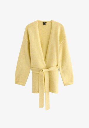 Keltainen neulottu neuletakki, jossa on V-pääntie, pitkät hihat ja yhteensopiva vyö. Ominaisuuksina ribbireunat ja pehmeä rakenne.