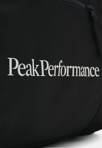 Bolsa de tela negra con el logo "PeakPerformance" en blanco. El diseño incluye una textura suave y un cierre con cremallera.
