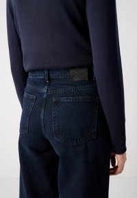 Donkerblauwe denim jeans met een slim fit, voorzien van een textuurband, twee achterzakken en een zwart logo op de achterkant van de taille.