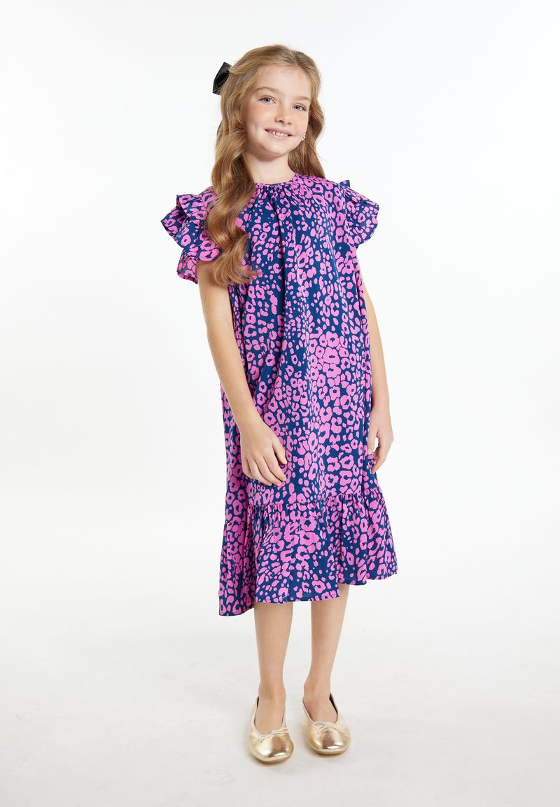 Rožinės ir mėlynos leopardų rašto suknelė su raukšlėtomis rankovėmis ir kelių lygių apatiniu kraštu. Modelis vilki auksines slidžias batus, stovintis ant balto fono.