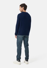 Marineblauer Pullover mit geripptem Muster, Rundhalsausschnitt und langen Ärmeln, kombiniert mit hellblauen Jeans und weißen Sneakers mit schwarzen Akzenten.