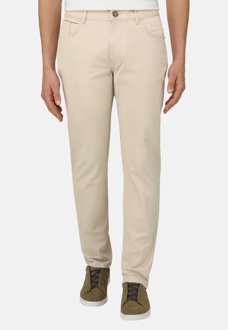 Homme portant un pantalon beige slim-fit et des baskets vert olive avec des lacets noirs, debout devant un fond uni.