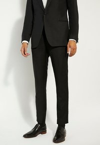 Pantalons de costume noirs à coupe slim. Fabriqués en tissu lisse, avec une taille plate, des passants de ceinture, et associés à des chaussures noires à lacets.