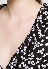 Černá látka s bílým vzorem srdcí, která má volánkový výstřih a hladký povrch, zdůrazňuje květinový design.