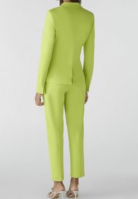 Costume ajusté vert citron avec une veste cintrée et un pantalon droit. Tissu lisse, coutures minimales et silhouette épurée.