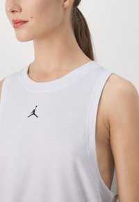 Valge ilma varrukateta sporditop ümmarguse kaeluse ja võrgust kangaga. Rinnal on must Jordan'i logo. Sujuv tekstuur ja mugav lõige.