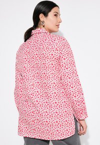Letvægts skjorte med pink blomsterprint, med krave, lange ærmer og sideslids. Materialet virker glat med en blød tekstur.