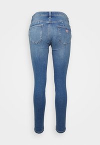 Jeans ajustados de denim azul medio con un acabado desgastado, que cuentan con dos bolsillos traseros y un parche con el logo en la cinturilla.