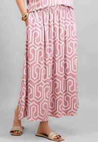 Fustă maxi roz cu model geometric alb, talie elastică, buzunare laterale și material ușor; asortată cu sandale împletite.