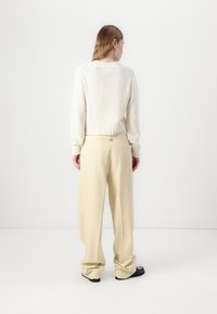 Pull en tricot crème noué avec un ourlet côtelé, associé à un pantalon large beige clair, doté de poches lat�érales et d'une silhouette épurée.
