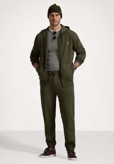 Olivno zeleni hoodie in športne hlače iz mehkega blaga s prilegajočim krojem, z zadrgo spredaj in majhnim logotipom. Združeno s temnim beanie klobukom.