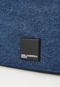 Denim fabric in varying shades of blue, featuring a square black label with "KARL LAGERFELD JEANS" in white text.