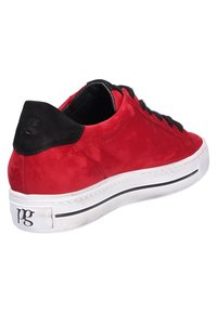 Baskets basses rouges avec languette de talon noire, lacets noirs, semelle blanche avec une bande noire et logo "pg" sur le bord extérieur du talon.