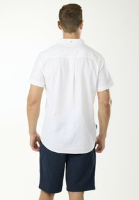 Weißes, kurzärmliges Hemd aus leichtem Stoff, mit einem Knopfkragen und einem abgerundeten Saum, kombiniert mit marineblauen Shorts.