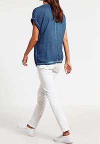 Denimowa bluzka z krótkim rękawem, niebieski kolor, luźny krój. W zestawie z białymi dżinsami z podwijanymi mankietami i białymi butami wsuwanymi. Prosty design.