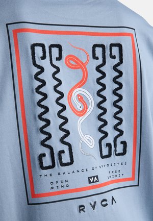 Deux serpents entremêlés, un rouge et un blanc, encadrés par des lignes zigzag noires et une bordure rouge, avec un texte sur l'équilibre et la liberté sur un tissu bleu.