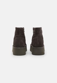 Bottines en daim marron avec une semelle plateforme en caoutchouc vert et bas, présentant une fermeture éclair latérale et des détails de couture pour ajouter de la texture.