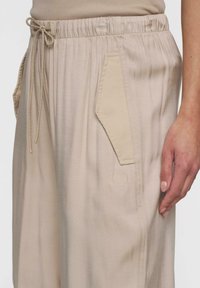 Beige casual fit broek met zijzakken en een trekkoord in de taille. Kenmerkt zich door een subtiele textuur en geborduurd nummer "10" op de zijkant.