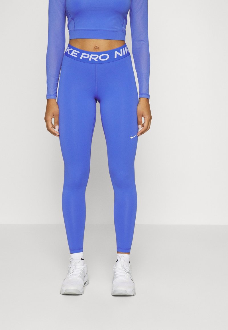 Blå Nike Pro tights med en tajt passform, slät textur och en kontrasterande vit midja med "NIKE PRO"-logotyp. Vita Nike-skor nedanför.