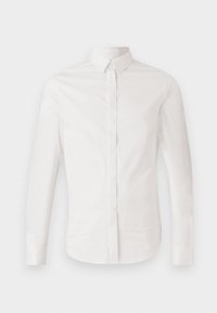 Chemise blanche à manches longues avec boutons et col pointu, présentée sur un fond clair uni.