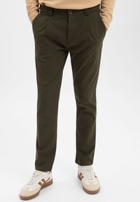 Khaki groene broek met een rechte snit, geplooide voorkant en riemlussen. Gecombineerd met beige en bruine sneakers met een gestructureerd ontwerp.